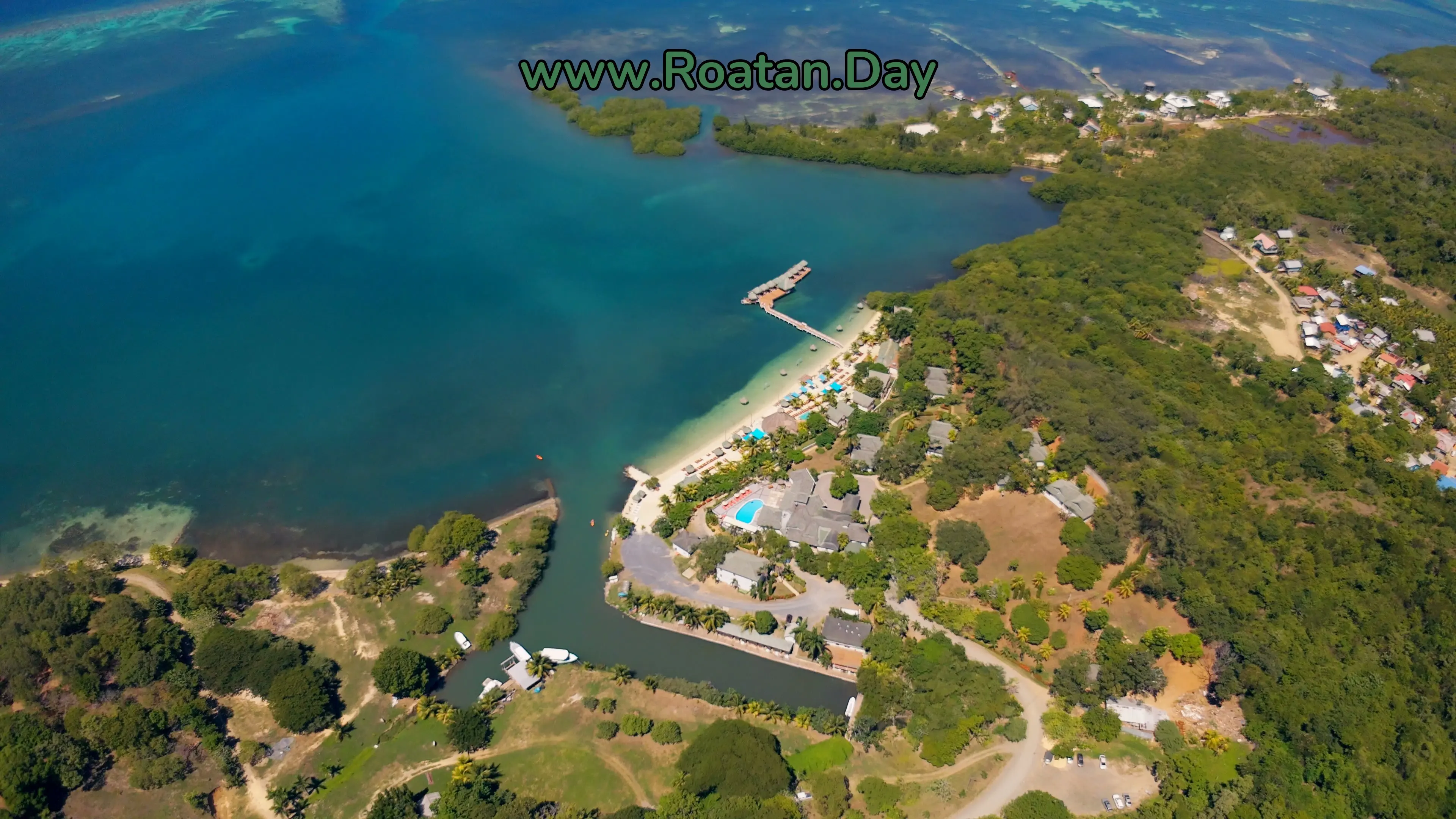 Turquoise Bay, Roatán, vue du ciel : la baie, la plage et son quai de bungalows sur l'eau, la piscine et le canal