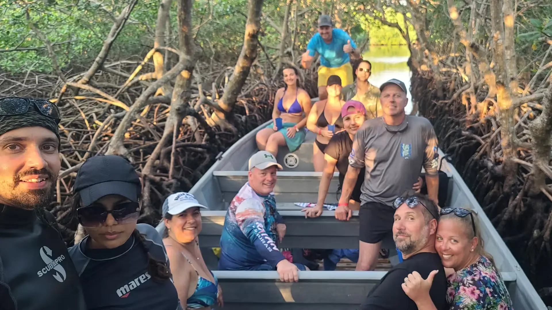 A boat full of tourist smiling at the camera inside a mangrove tunnel during sunset